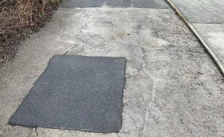 A patch of darker tarmac covers a square section of lighter pavement.