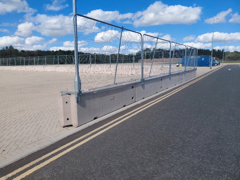 Heras fence panels mounted on concrete barriers using bolt-over brackets and supporting braces