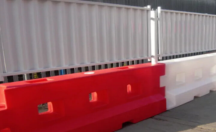 Red and white plastic barriers with interlocking design alongside a corrugated metal fence.