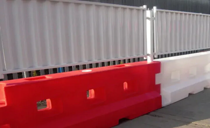Red and white plastic barriers with interlocking design alongside a corrugated metal fence.