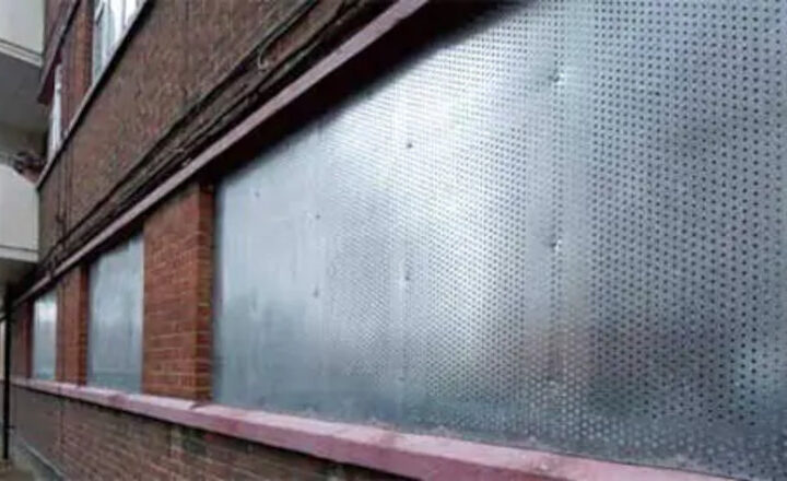 Perforated metal panels covering windows on a red brick building exterior.