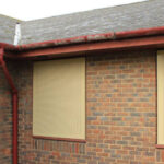 Brick building with boarded windows, red guttering, and moss on pitched roof.