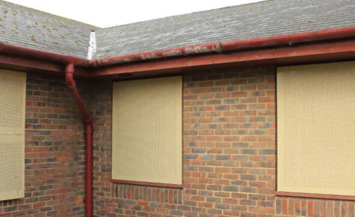 Brick building with boarded windows, red guttering, and moss on pitched roof.