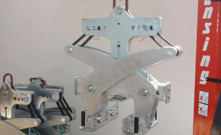 Suspended industrial metal clamp mechanism with springs, mounted on an orange vertical structure.