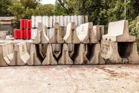 Concrete barriers stacked in multiple rows, including red and white sections, on a paved surface.