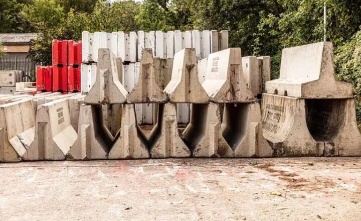 Concrete barriers stacked in multiple rows, including red and white sections, on a paved surface.