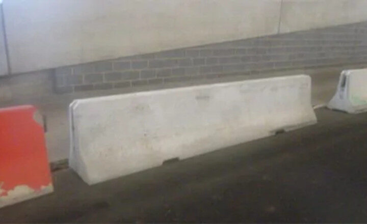 Concrete and plastic barriers line a road next to a brick and concrete wall.