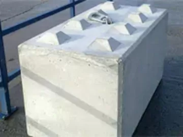 Concrete block with pyramidal protrusions on top, placed on an outdoor pavement.