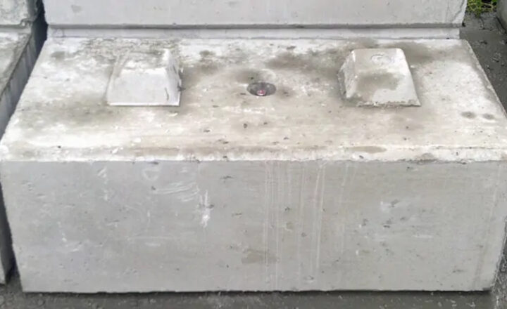 Concrete block with raised sections and a central circular metal feature on its surface.