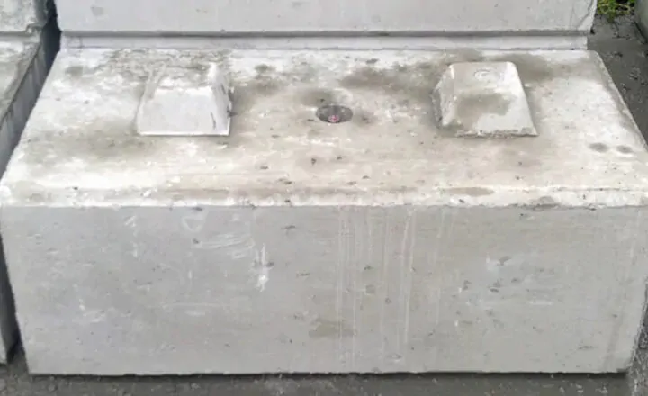 Concrete block with raised sections and a central circular metal feature on its surface.