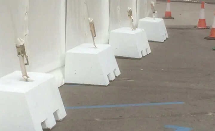 White barriers anchored with weights alongside traffic cones on a pavement.