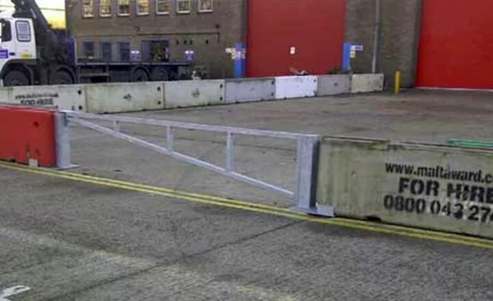 Concrete and metal barriers installed on a road, with a truck and building background.