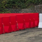 Red and white concrete traffic barriers lined up outdoors on a gravel surface