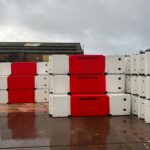 Stacked red and white concrete traffic barriers with directional arrows in a storage yard